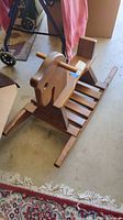 Front side view of child's wooden rocking horse showing horse head with hand grips, slatted seat, and curved rockers.
