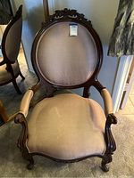 Front view of an oval back wood frame salon chair with carved details and light beige striped upholstery