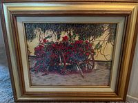 Framed signed print showing a wooden cart filled with red flowers under tree branches, photographed head-on.