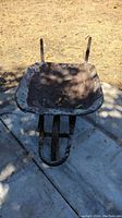 Front angled view of vintage metal wheelbarrow showing deep rusted square basin and wheel.