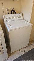 Full view of white Kenmore top-loading washing machine placed next to another appliance, showing general shape and condition with rust and wear.