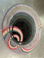 Full view of the round carpet showing colorful concentric circular pattern on a concrete floor.