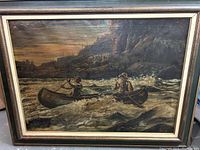 Full frontal photo of the oil painting showing two men canoeing in turbulent water with a rocky shoreline in the background, framed in black wood with gold trim and inner white border.