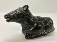 Front and partial side view of the black stone Inuit carving showing animal head and body details.