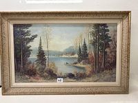 Full view of the framed landscape oil painting showing the lake, trees, and cabin with signature visible.
