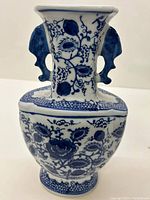 Front view of the blue and white ceramic vase showing floral designs and ornamental handles near the neck.