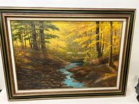 Full view of the framed oil on board painting showing the forest scene with a stream and autumn colors.