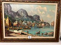 Front view of framed coastal oil painting showing fishing boats in a harbor with mountainous village backdrop