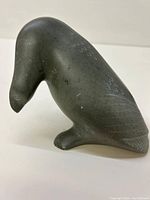 Side view of dark gray soapstone bird carving showing curved head and incised feather design.
