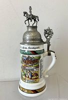 Front-side view of the beer stein showing painted regimental scenes and the mounted soldier figure on the pewter lid.