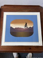 Photo of framed lithograph showing the entire artwork on a wooden surface.