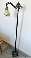 Full view of the vintage metal floor lamp showing the ornate bridge arm and base, and the feathered art glass shade hanging from the arm.