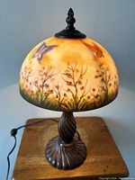 Full view of the table lamp showing painted floral and butterfly scene on glass dome shade and dark metal twisted base.