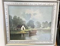 Framed oil painting showing a landscape with cabin by lake and boats, signed by artist 'Souren'.