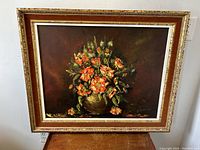 Frontal image of the gilt wood framed impressionist floral oil painting on canvas. Dark background, orange and pink flowers in a vase, signed by Jimoski.
