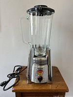Front view of the blender showing the glass jar and chrome metal base with power cord coiled behind.