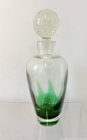 Front view of clear glass decanter showing green flame color pattern from base upwards and glass stopper on top.