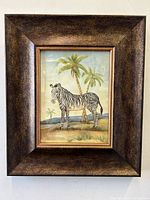 Front view of the framed art print featuring a zebra in a natural landscape with palm trees, encased in a brown wooden frame