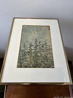 Framed watercolour artwork of trees with crystallization on top left, displayed on a wooden surface against blank wall.