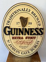 Front view of oval Guinness wooden sign showing brand text, harp logo, and traditional brewing information.