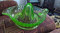 Side angled view showing the bright green fluorescent bright Vaseline glass lemon juicer with Art Deco fluted ridged reamer in the center, dual spouts, and oval bowl shape.