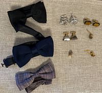 All items in the lot: three bowties, three pairs of cufflinks, and three tie pins laid out on beige fabric.