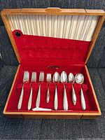 Photo of some forks and spoons arranged in red velvet slots inside a wooden box with cream satin lining in the lid.