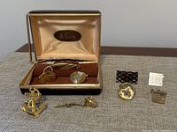 Set of assorted cufflinks and tie pins displayed on table including Di Gino set in case, anchor tie pin, and various metal cufflinks