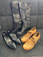 Photo showing all three pairs of shoes together: black Geox boots, black Ecco heels, and tan Clarks heels on a gray fabric sofa.