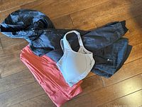 Three Lululemon clothing items including black jacket, grey sports bra, and coral leggings laid on wooden floor.