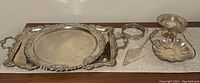 Full set of two silver plated serving trays, candy dish, handled dish, and cake server arranged on a shelf