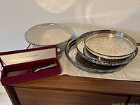 Silver plate cake stand, three serving trays stacked, and cake server case on wooden surface