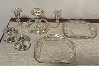 Photo showing two etched glass plates with silver floral designs and three silver plated candle holders including a three-arm candelabra and two single holders.