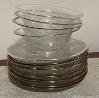 Stack of four vintage glass fruit bowls with etched designs and silver rims placed on top of eleven dessert plates with matching silver rims and etched patterns.