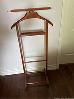 Full front view of vintage wooden butler valet stand on caster wheels, showing hanger, shelf and trouser bar