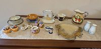 Full overview of the lot showing all ceramic items laid out on a table including small bowls, pitchers, teapot, salt and pepper shakers, and other small containers.