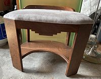 Front view showing wooden frame with stepped geometric detail and light gray upholstered cushion.