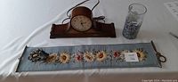 Overall view showing mantel clock, needlepoint bell pull with floral design, and an unrelated vase.