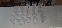 Full view of the assortment of crystal glasses arranged in rows on table showing variety of shapes and sizes