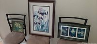 Iris floral print leaning on the wall beside a chair with two other framed prints, showing size and framing.