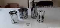 Four-piece bathroom set on a table including soap dispenser, toothbrush holder, cotton ball holder with lid, and glass tumbler in black and white speckled glass design.