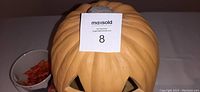 Single image showing top and facial carving of the plastic illuminated pumpkin in orange color with MaxSold lot sticker.