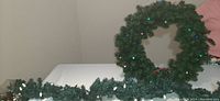 Photo showing the artificial evergreen garland laid out on table alongside wreath, lights visible on wreath.