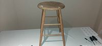 Full view of the oak work stool showing round seat, four legs, and stretchers, on white table, some paint marks on seat.