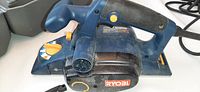 Blue and black Ryobi electric power planer with ergonomic handle, chip ejection control, and yellow depth adjustment knob.
