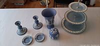 Full view of all items in the Wedgwood jasperware set on a table; includes candlesticks, ashtrays, sugar bowl, vase, and three-tiered plate.