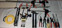 Full view of lot showing various clamps, wood chisels, hammers, tin snips, wrecking bars, and wire fish tape arranged on surface.