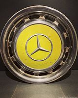 Front view of 1938 Mercedes Benz hubcap showing yellow center with star logo and chrome rim with oval cutouts.