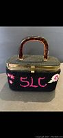 Front view of black box purse showing floral embroidery and pink 'SLC' lettering, brass-toned rim, and tortoiseshell Bakelite handle.