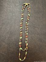 Full view of the long double strand beaded necklace laid flat showing the multicolored speckled glass beads in autumnal tones.